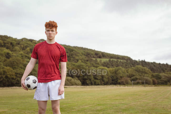 Jeune footballeur debout avec un ballon de football sur le terrain — Photo de stock