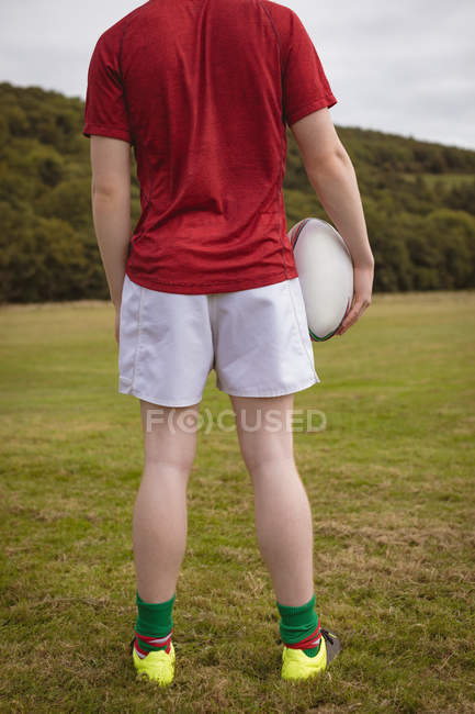 Vue arrière du joueur de rugby debout avec une balle de rugby sur le terrain — Photo de stock