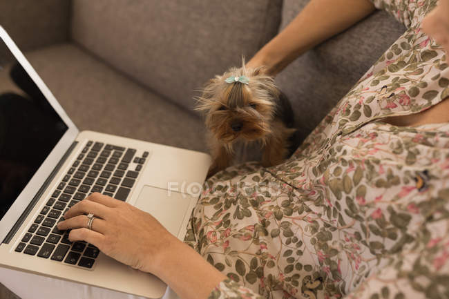 Frau benutzt Laptop, während sie ihren Hund zu Hause streichelt — Stockfoto