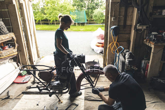 Чоловічі та жіночі механіки ремонтують мотоцикл у ремонтному гаражі — стокове фото