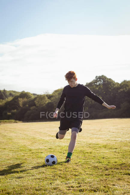 Jogador de futebol chutando futebol no campo em um dia ensolarado — Fotografia de Stock
