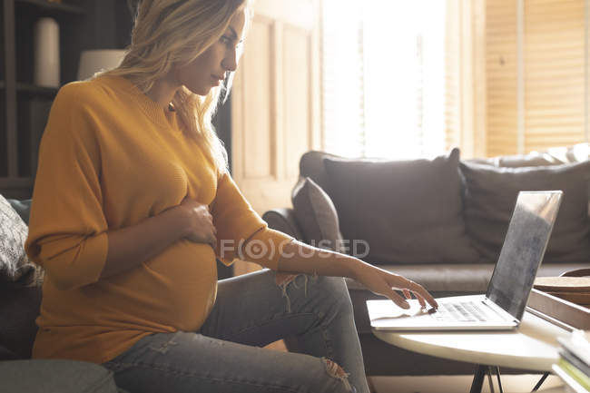 Концентрированная беременная женщина с ноутбуком дома — стоковое фото