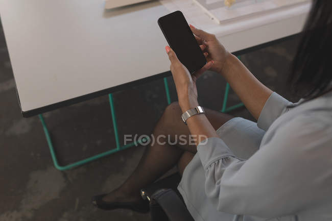 Female executive using mobile phone at table in office — Stock Photo
