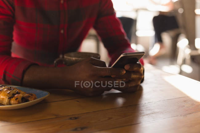 Средняя секция человека с помощью мобильного телефона в кафе — стоковое фото