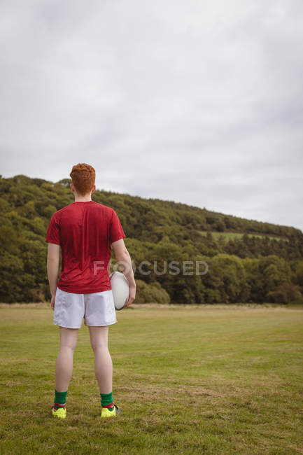 Visão traseira do jogador de rugby de pé com bola de rugby no campo — Fotografia de Stock