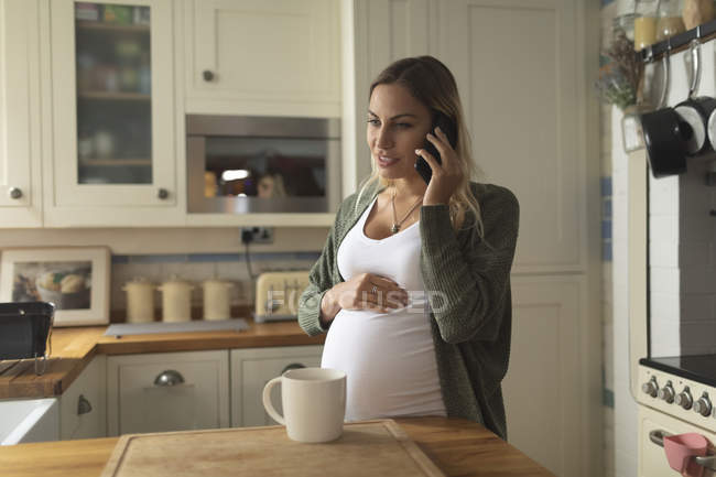 Femme enceinte parlant au téléphone dans la cuisine à la maison — Photo de stock