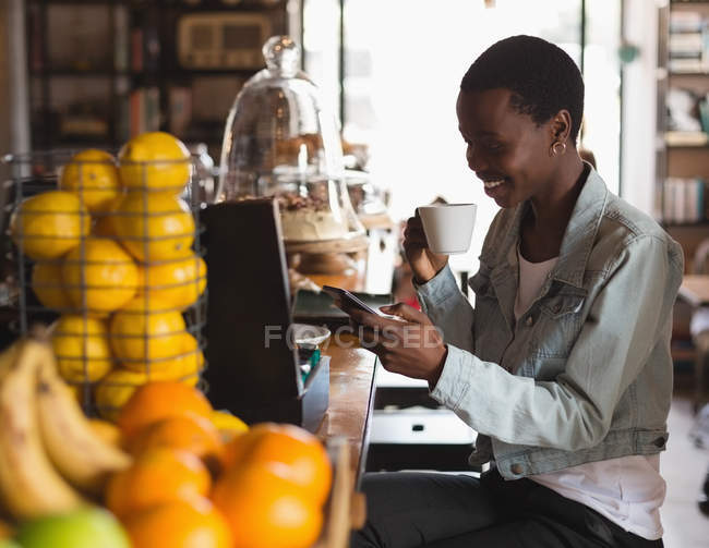 Щаслива жінка використовує мобільний телефон, маючи каву в кафе — стокове фото