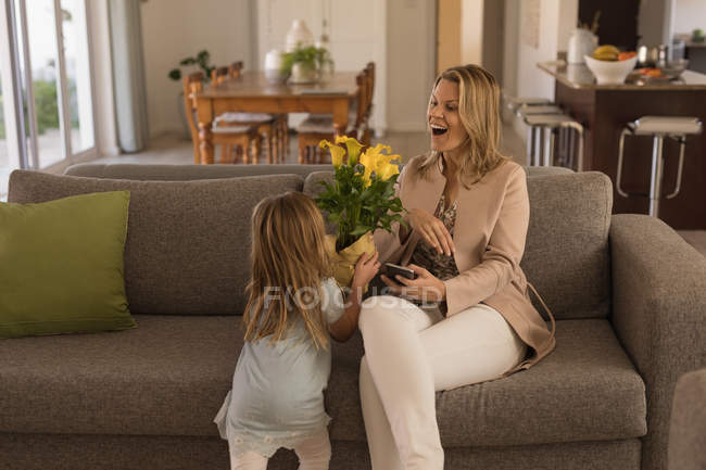 Fille donnant bouquet de fleurs à sa mère dans le salon à la maison — Photo de stock