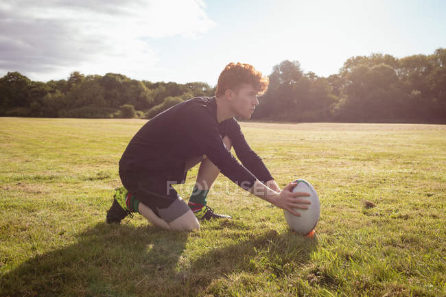 Jugador de rugby colocando pelota de rugby en el campo en un día soleado - foto de stock