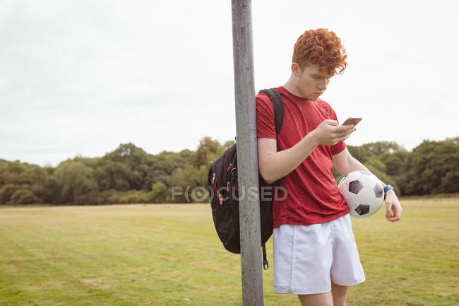 Giovane giocatore di calcio che utilizza il telefono cellulare sul campo — Foto stock