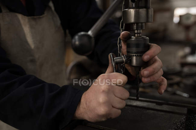 Primer plano del herrero utilizando taladro de prensa en el taller - foto de stock