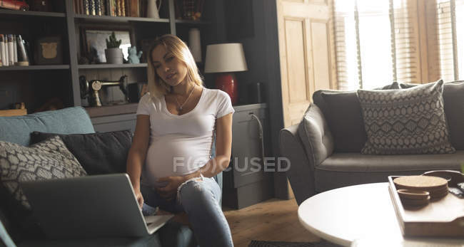 Mujer embarazada usando el ordenador portátil en casa - foto de stock