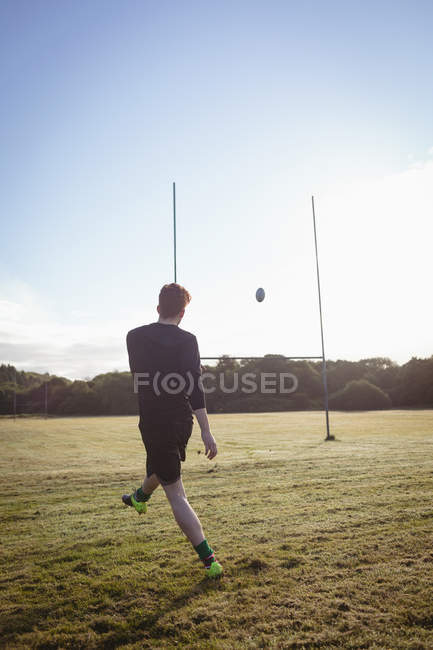 Jogador de rugby chutando bola de rugby no campo em um dia ensolarado — Fotografia de Stock