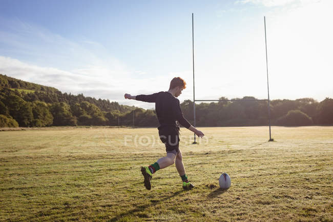 Joueur de rugby donnant un coup de pied au ballon de rugby sur le terrain par une journée ensoleillée — Photo de stock
