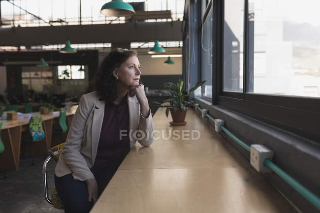 Thoughtful woman looking through window in office — Stock Photo
