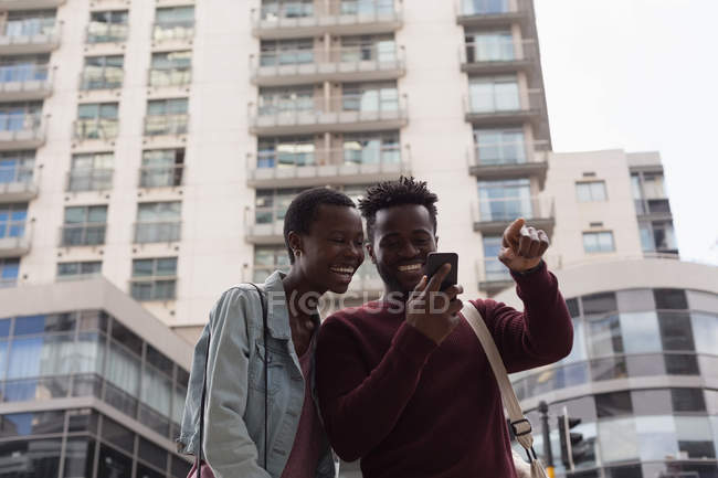 Couple heureux utilisant le téléphone mobile dans la rue de la ville — Photo de stock