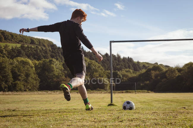 Jogador de futebol chutando futebol no campo em um dia ensolarado — Fotografia de Stock