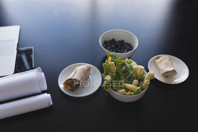 Alimentos saudáveis dispostos em tigela e prato no escritório — Fotografia de Stock