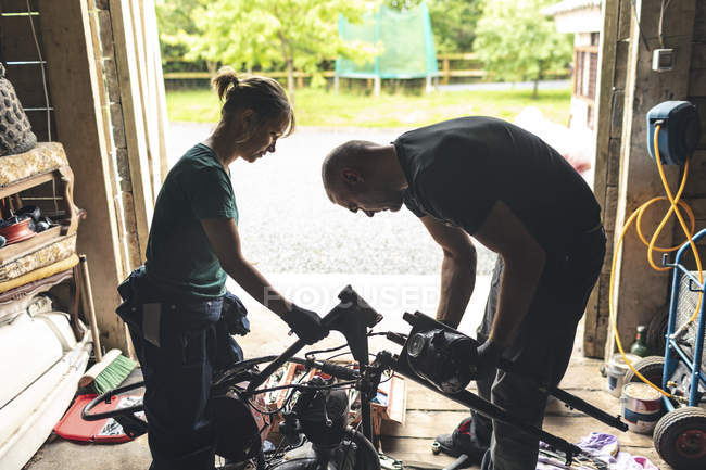 Mécaniciens masculins et féminins réparer moto dans le garage de réparation — Photo de stock