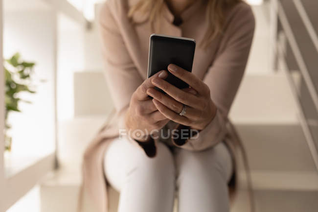 Sección media de la mujer usando el teléfono móvil en las escaleras en casa - foto de stock
