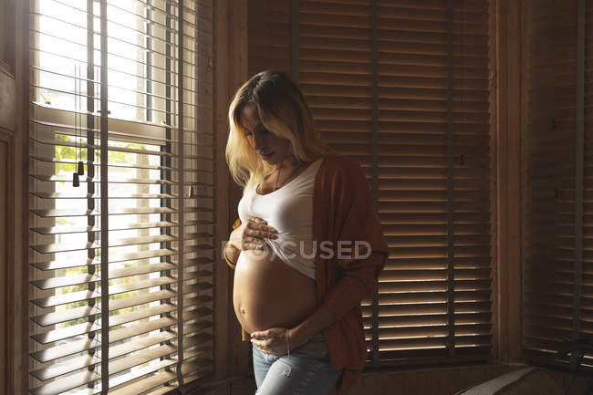 Pregnant woman touching her belly near the window at home — Stock Photo