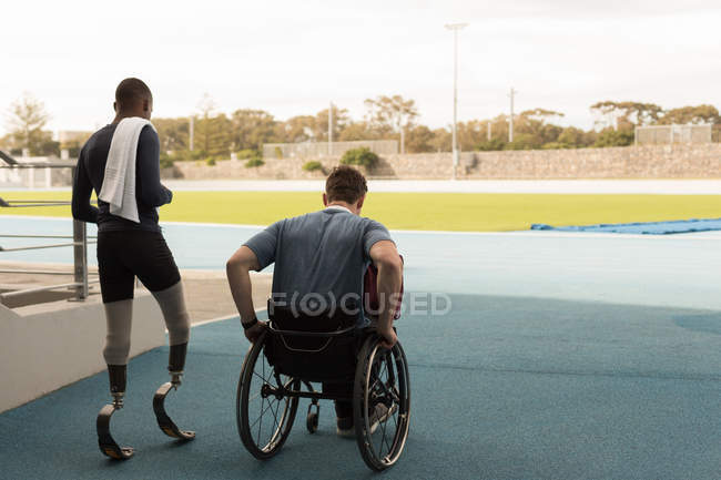 Visão traseira de dois atletas com deficiência andando juntos em um local esportivo — Fotografia de Stock