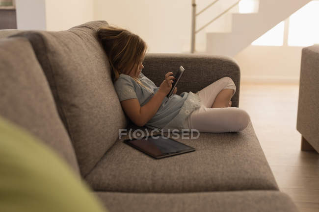 Chica usando el teléfono móvil en la sala de estar en casa - foto de stock