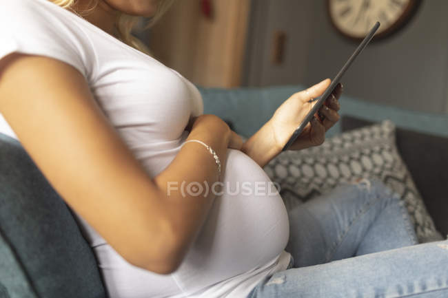 Середина вагітної жінки, використовуючи цифровий планшет на дивані — стокове фото