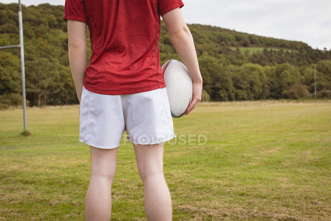 Mid section of rugby player standing with rugby ball in the field — Stock Photo