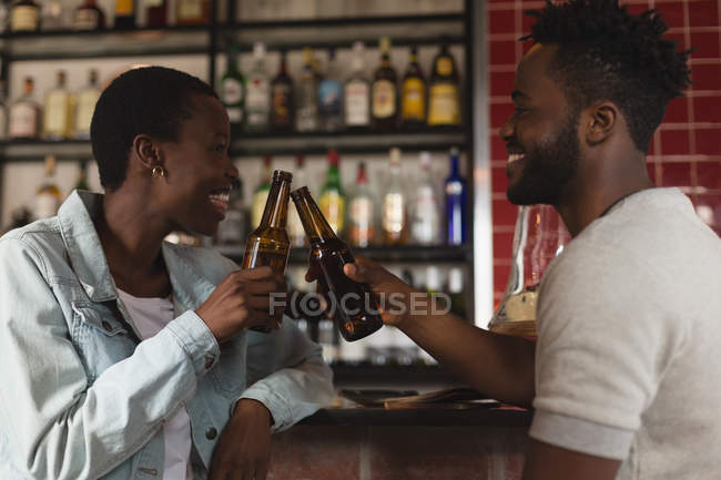 Feliz pareja tostando botella de cerveza en la cafetería - foto de stock