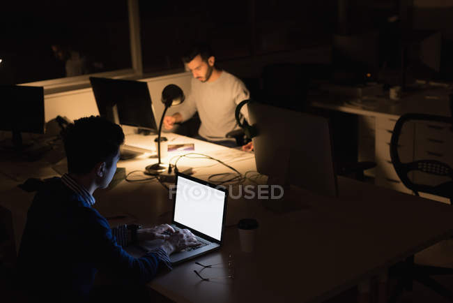Dos hombres de negocios trabajando en el ordenador portátil en la oficina durante la noche - foto de stock