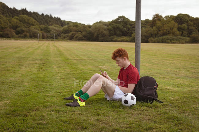 Молодий футболіст використовує мобільний телефон у полі — стокове фото