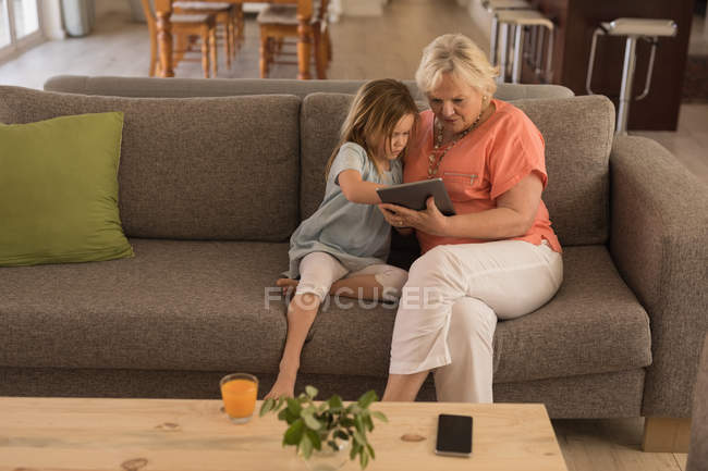 Abuela y nieta usando tableta digital en la sala de estar en casa - foto de stock
