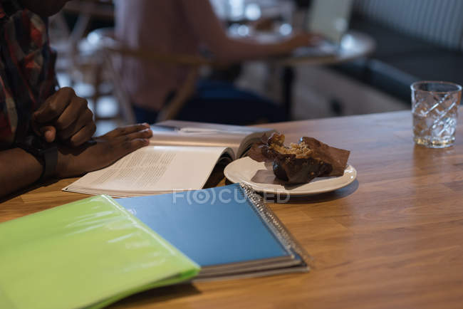 Teller mit Nachtisch und Geschäftsmann liest ein Buch in Cafeteria im Büro — Stockfoto