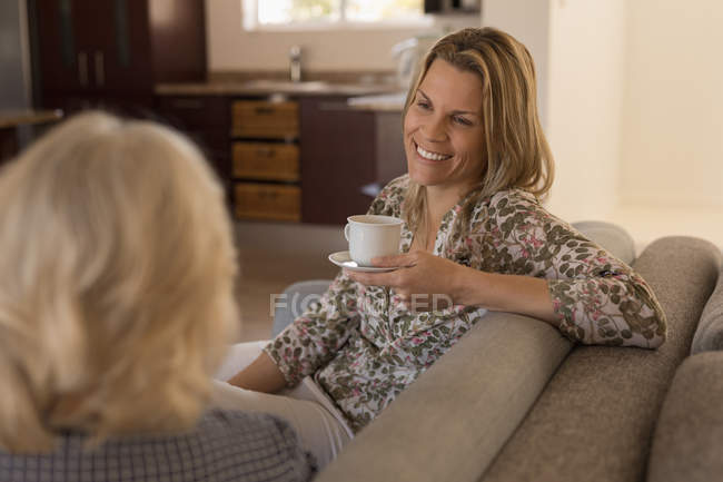 Mãe e filha interagindo uns com os outros enquanto toma café na sala de estar em casa — Fotografia de Stock