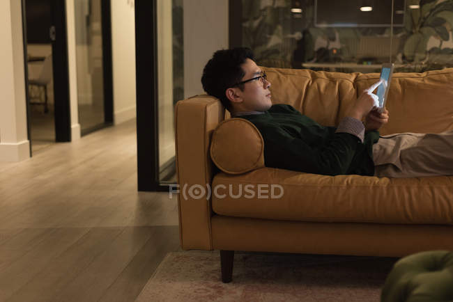 Homme d'affaires concentré couché sur un canapé et utilisant une tablette numérique — Photo de stock