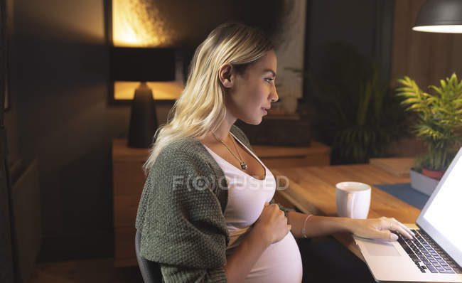 Femme enceinte concentrée utilisant un ordinateur portable à la maison — Photo de stock