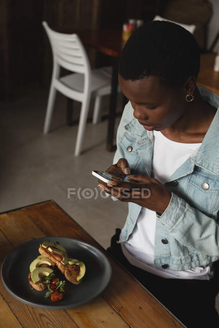 Mujer tomando fotos de la comida en la cafetería - foto de stock