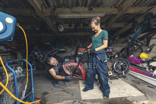 Механики мужского и женского пола ремонтируют мотоцикл в ремонтном гараже — стоковое фото