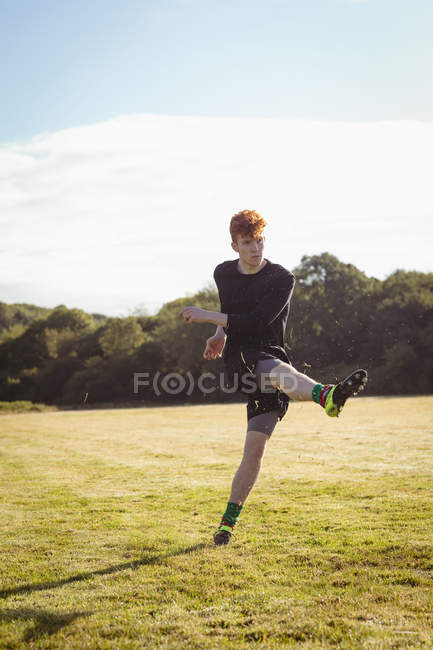 Футболист, пинающий футбол в поле в солнечный день — стоковое фото