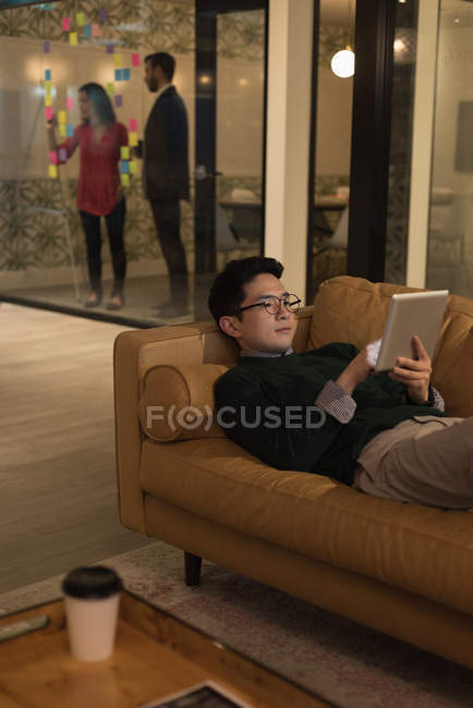 Концентрированный бизнесмен лежит на диване и использует цифровой планшет — стоковое фото