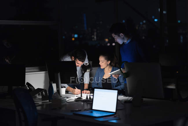 Три бізнесмени працюють на ноутбуці в офісі в нічний час — стокове фото