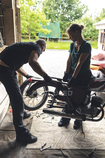 Meccanici di sesso maschile e femminile che riparano moto in officina — Foto stock