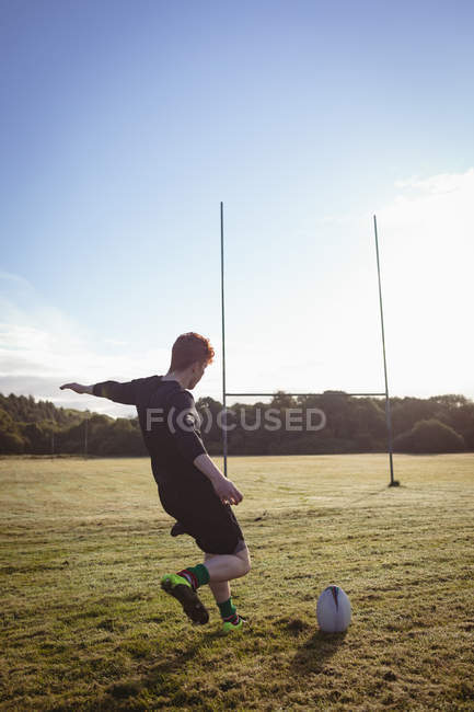Joueur de rugby donnant un coup de pied au ballon de rugby sur le terrain par une journée ensoleillée — Photo de stock