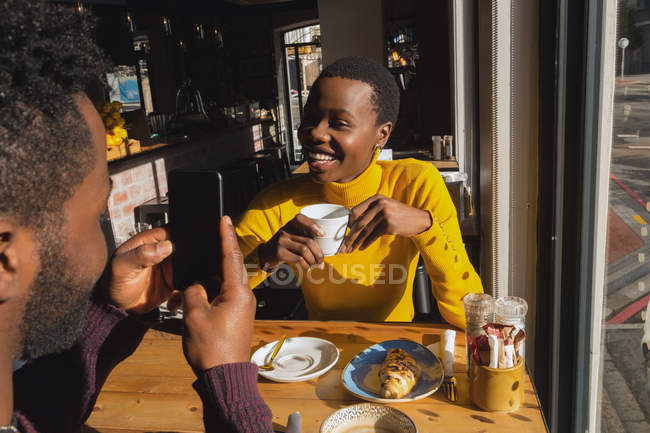 Hombre feliz tomando fotos de la mujer en la cafetería - foto de stock