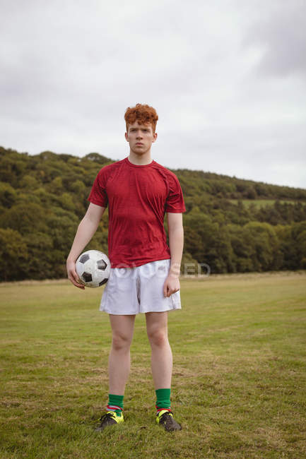Jovem jogador de futebol de pé com bola de futebol no campo — Fotografia de Stock