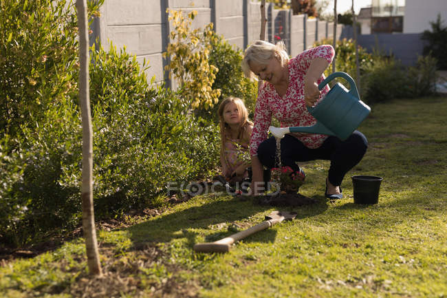 Abuela y nieta plantando en el jardín en un día soleado - foto de stock