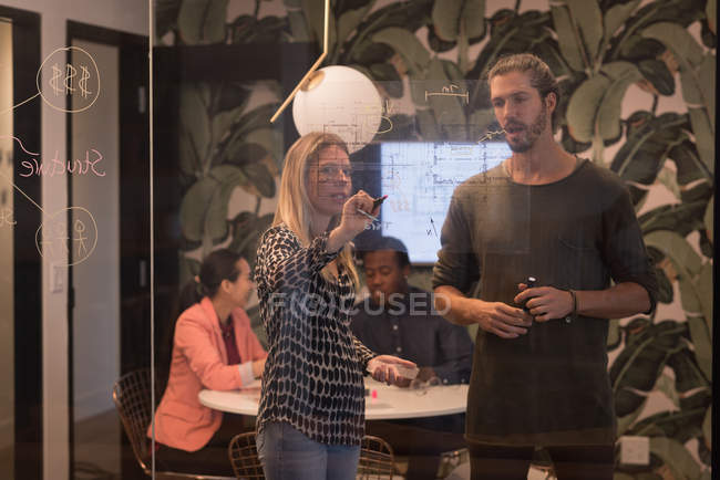Ділові люди обговорюють схему на скляній стіні в офісі — стокове фото