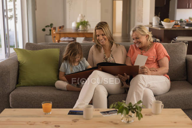 Multi-generation family looking at photo album in living room at home — Stock Photo