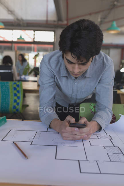 Male executive using mobile phone while working on blueprint in office — Stock Photo